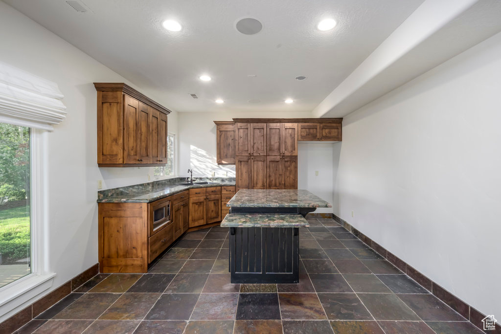 Kitchen with dark tile floors, a center island, sink, dark stone counters, and stainless steel microwave