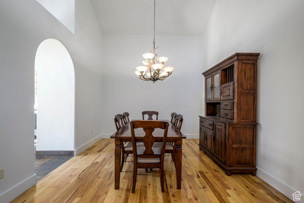 Dining area with light hardwood / wood-style flooring, high vaulted ceiling, and an inviting chandelier