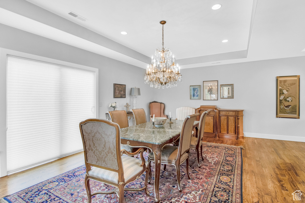 Dining room with light hardwood / wood-style floors, a chandelier, and a raised ceiling