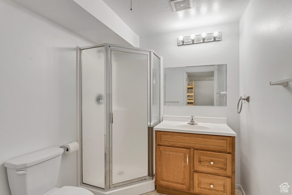 Bathroom with a shower with shower door, a textured ceiling, vanity, and toilet