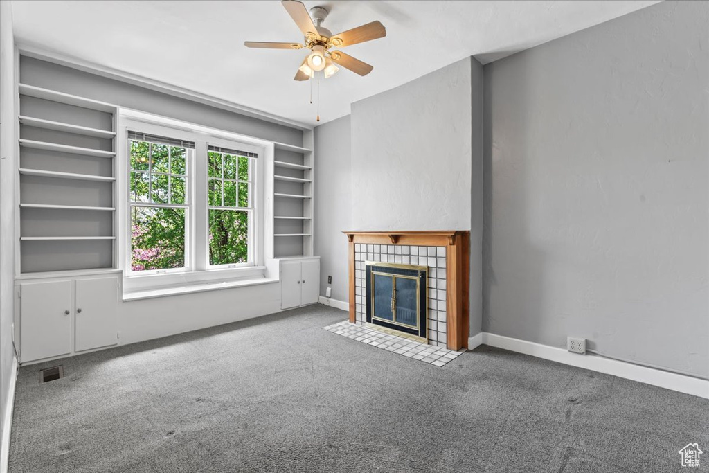Unfurnished living room with ceiling fan, a tile fireplace, carpet floors, and built in shelves