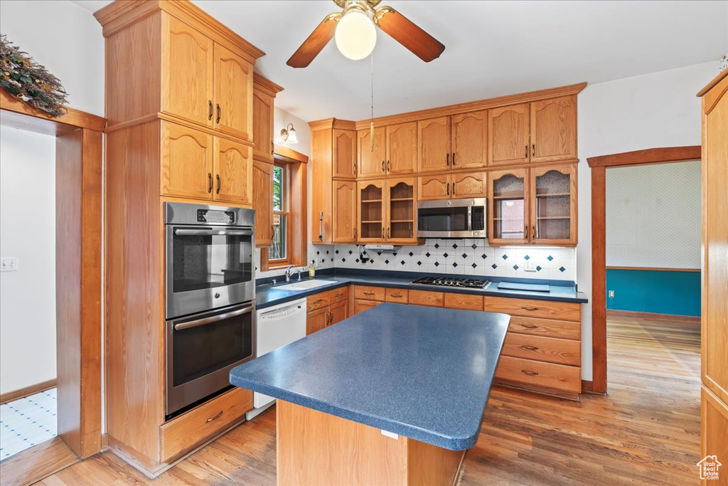 Kitchen with appliances with stainless steel finishes, a kitchen island, backsplash, ceiling fan, and wood-type flooring