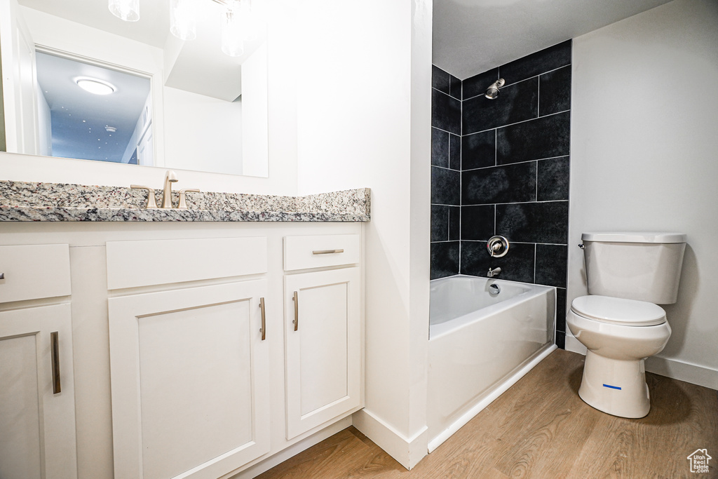 Full bathroom with hardwood / wood-style floors, tiled shower / bath, vanity, and toilet