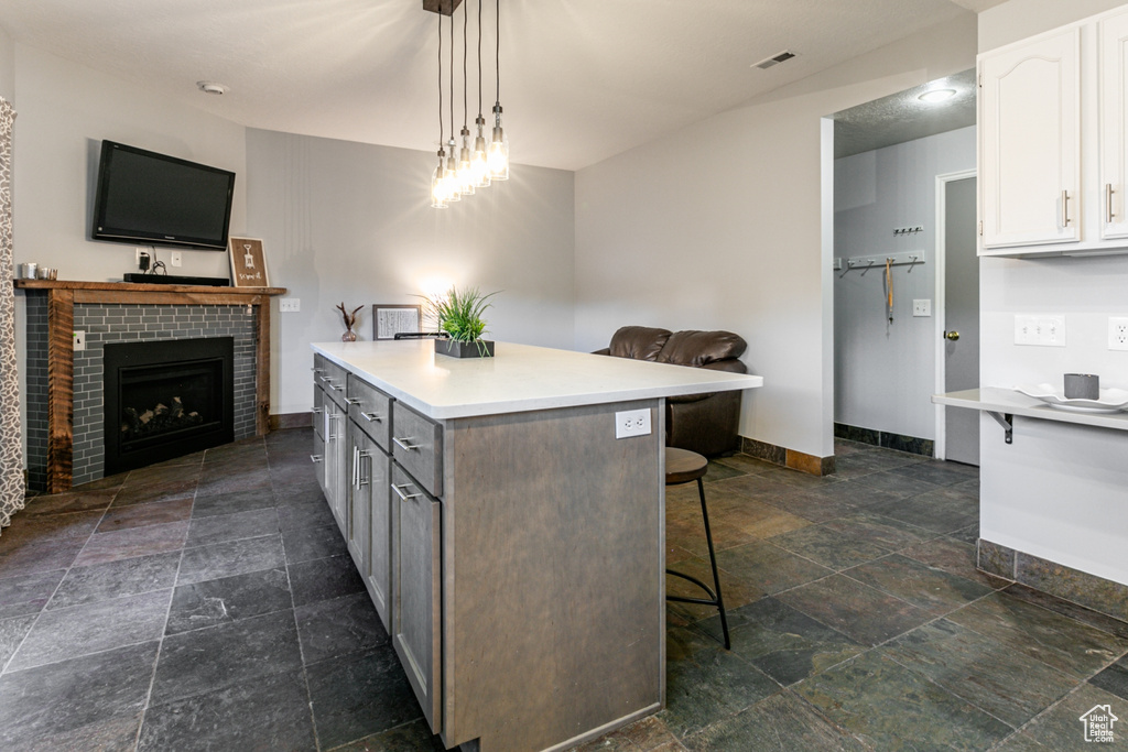 Kitchen featuring white cabinets, dark tile floors, pendant lighting, and a tiled fireplace