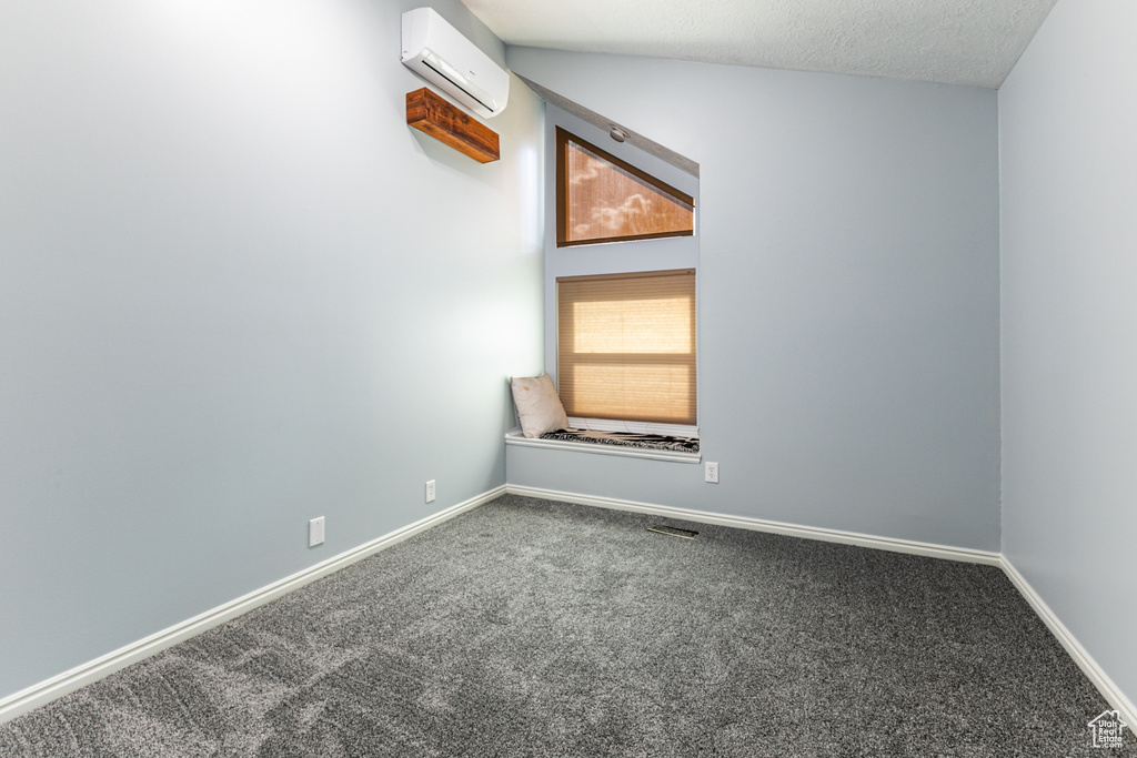 Carpeted spare room with lofted ceiling, an AC wall unit, and a textured ceiling
