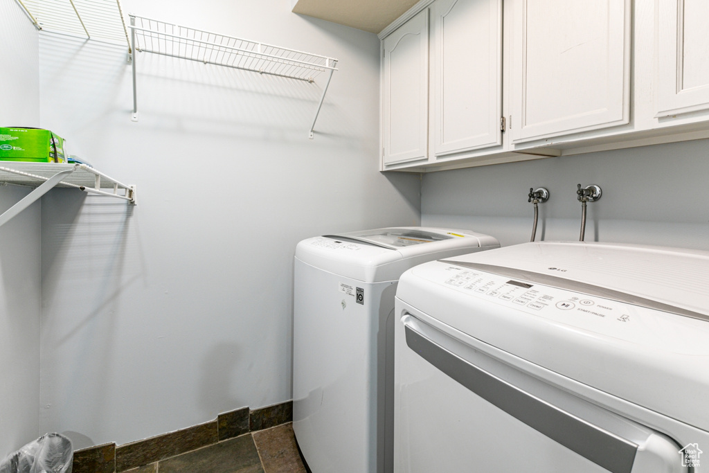 Clothes washing area with cabinets, hookup for a washing machine, dark tile flooring, and separate washer and dryer