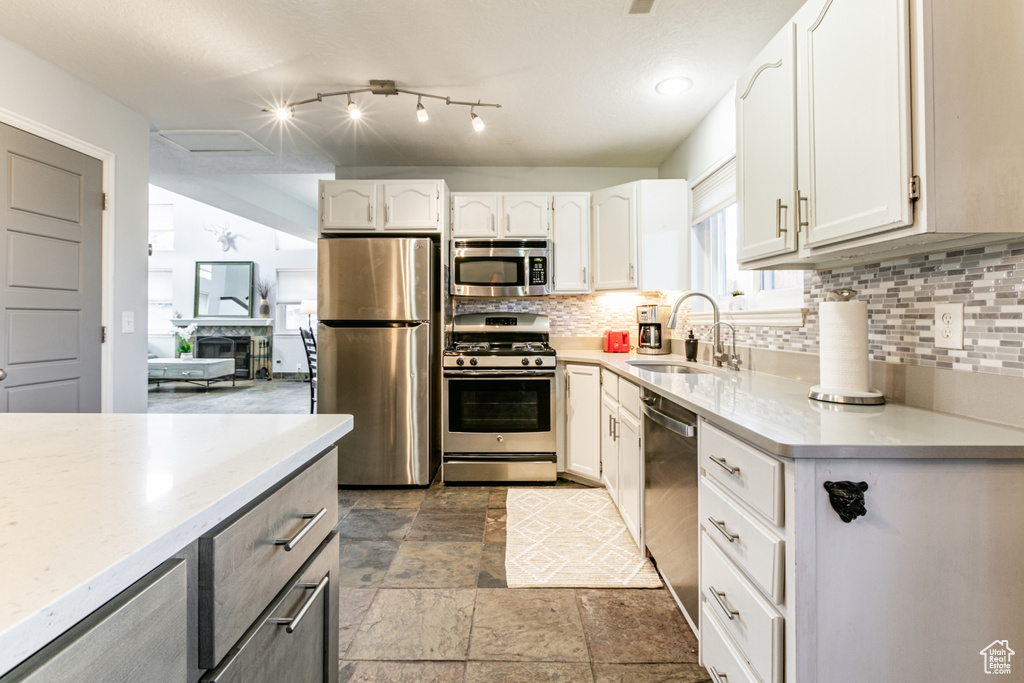 Kitchen featuring white cabinets, tile floors, stainless steel appliances, sink, and tasteful backsplash