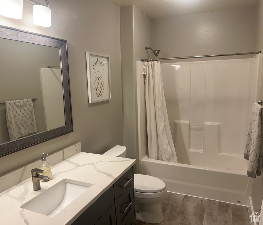 Full bathroom with hardwood / wood-style floors, large vanity, toilet, and shower / bath combo with shower curtain
