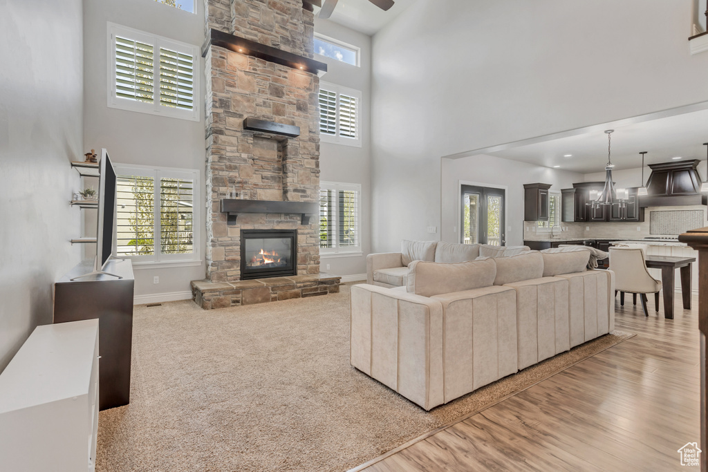 Living room featuring a wealth of natural light, carpet flooring, a stone fireplace, and a high ceiling