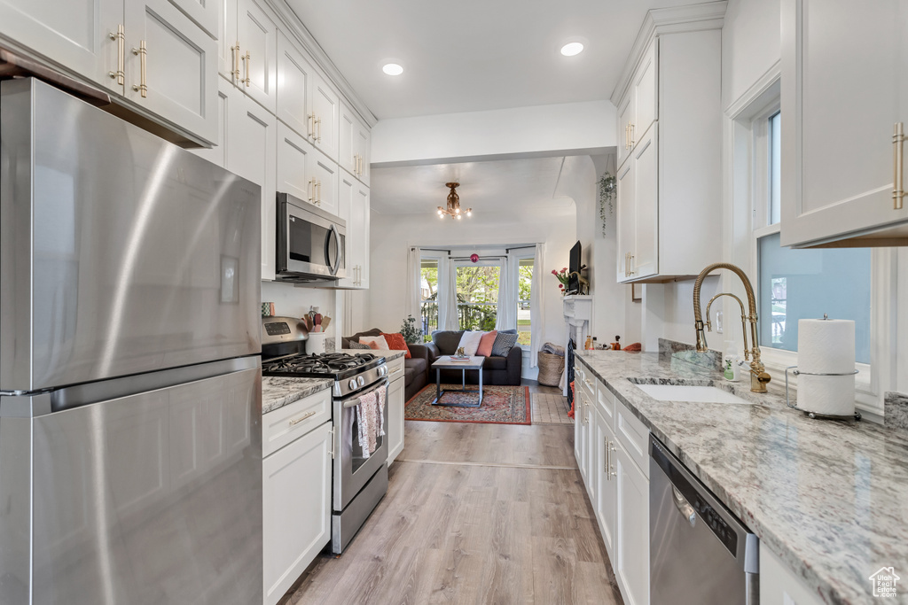 Kitchen featuring light stone countertops, appliances with stainless steel finishes, light hardwood / wood-style flooring, white cabinets, and sink