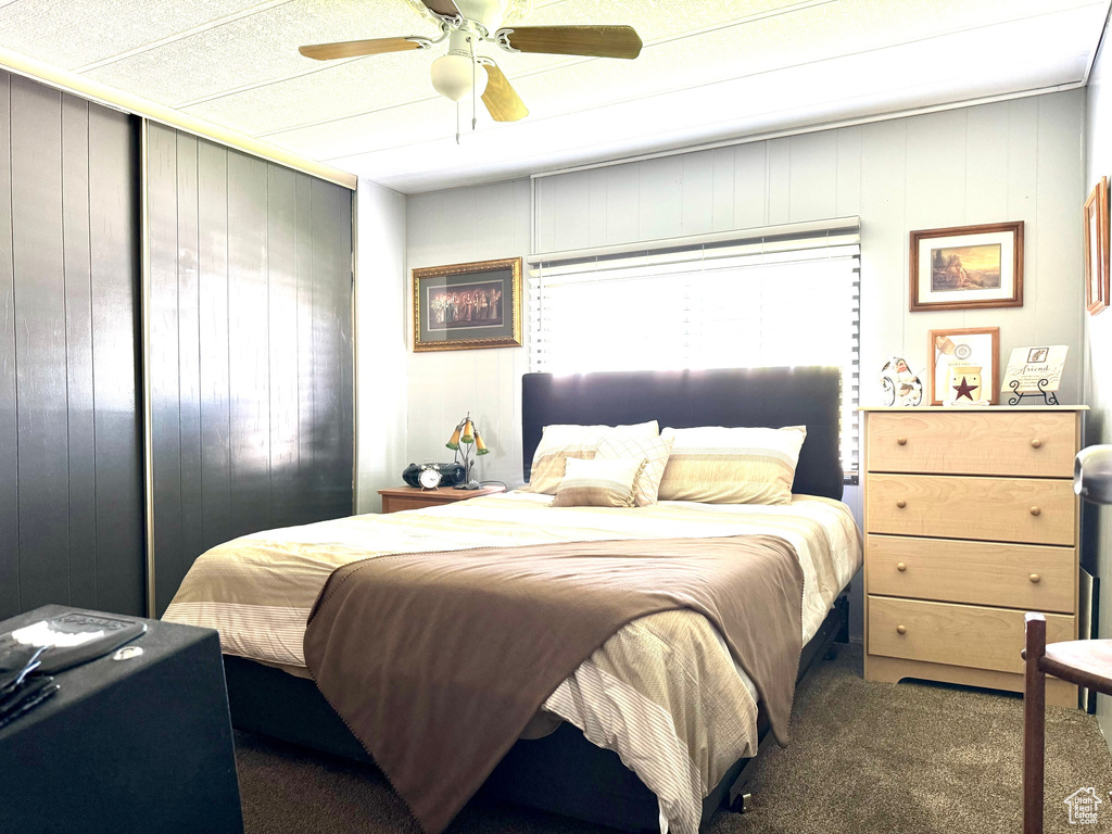 Bedroom featuring wooden walls, ceiling fan, and carpet floors