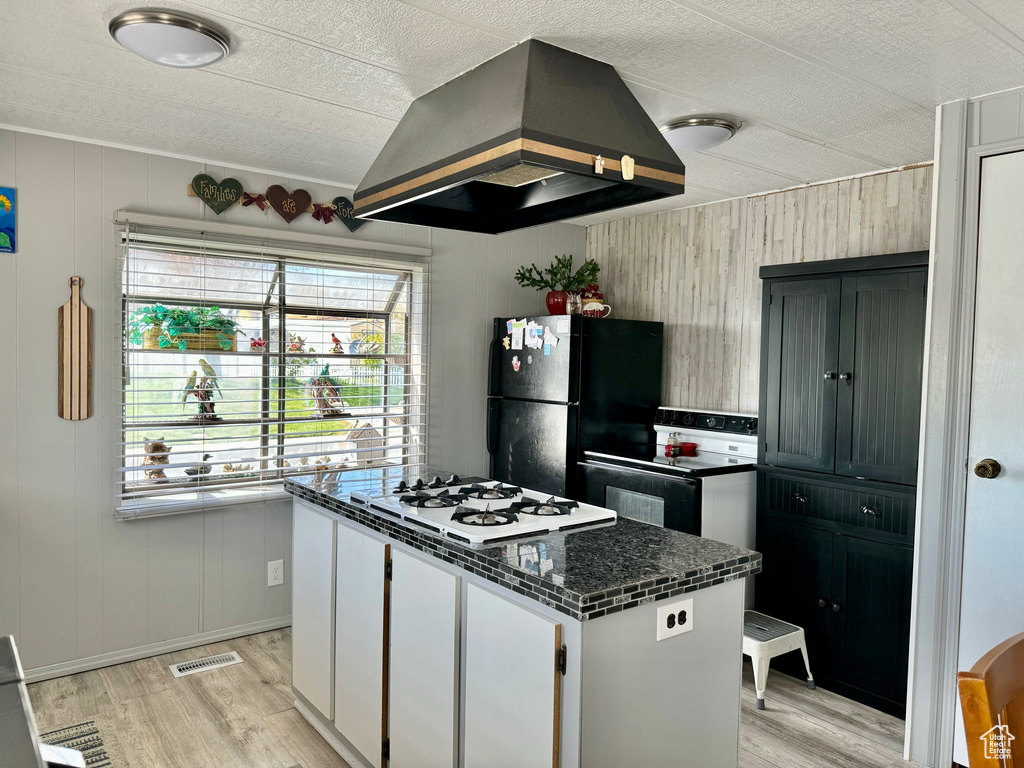 Kitchen featuring black fridge, island exhaust hood, white cabinetry, a center island, and light wood-type flooring