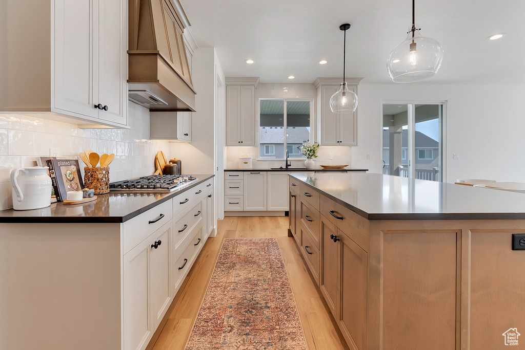 Kitchen featuring light wood-type flooring, a spacious island, premium range hood, and backsplash