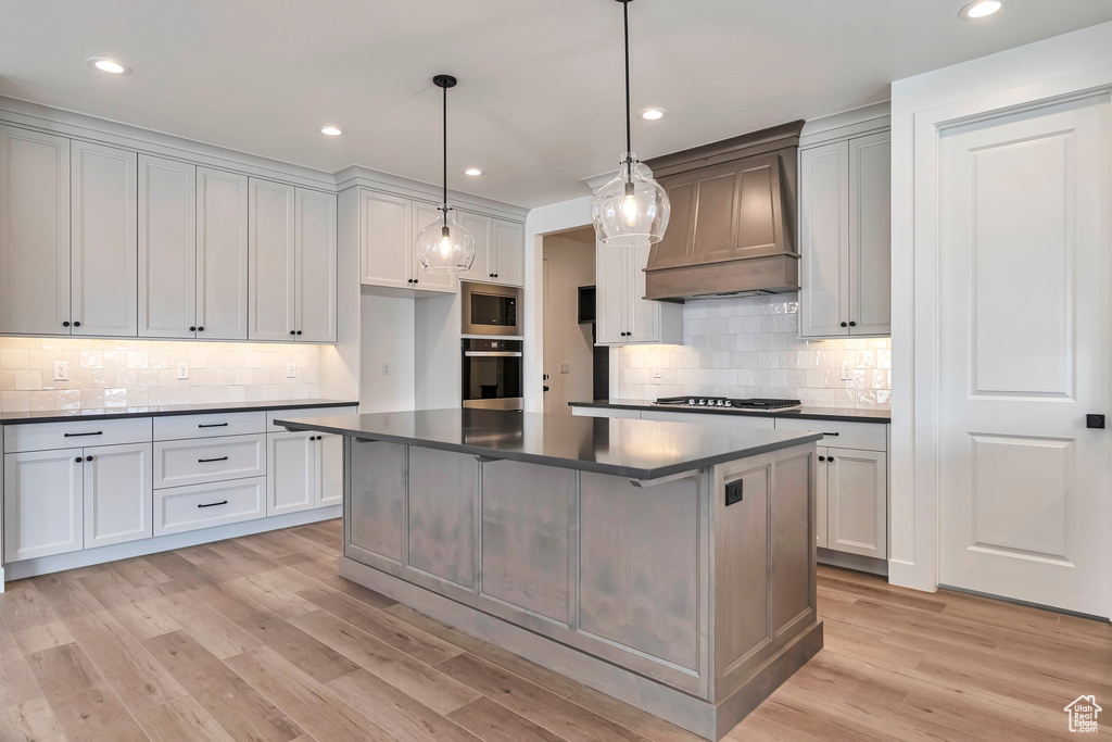 Kitchen featuring a center island, premium range hood, light wood-type flooring, backsplash, and appliances with stainless steel finishes