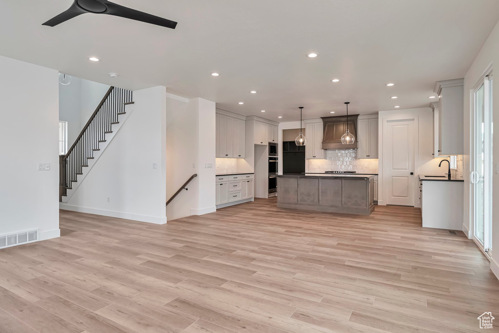 Kitchen with backsplash, light hardwood / wood-style flooring, custom exhaust hood, pendant lighting, and a center island