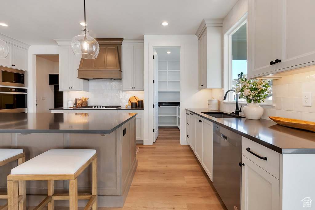 Kitchen featuring backsplash, stainless steel appliances, light hardwood / wood-style floors, custom exhaust hood, and sink