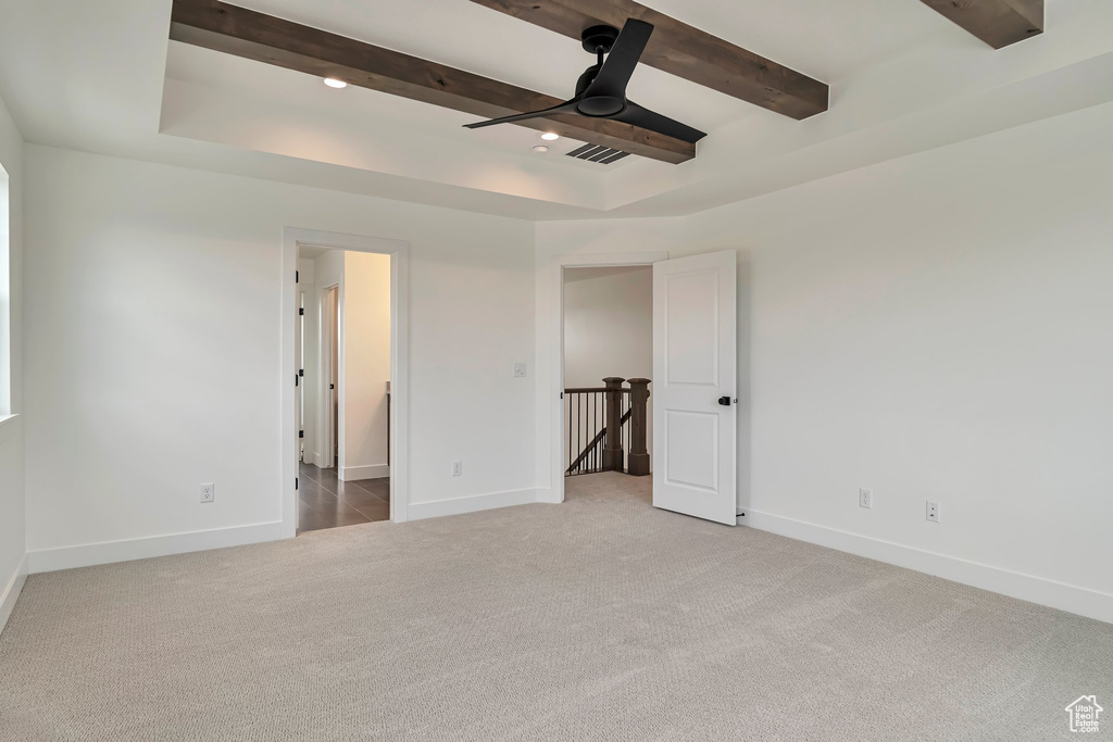 Carpeted empty room featuring beamed ceiling, ceiling fan, and a tray ceiling