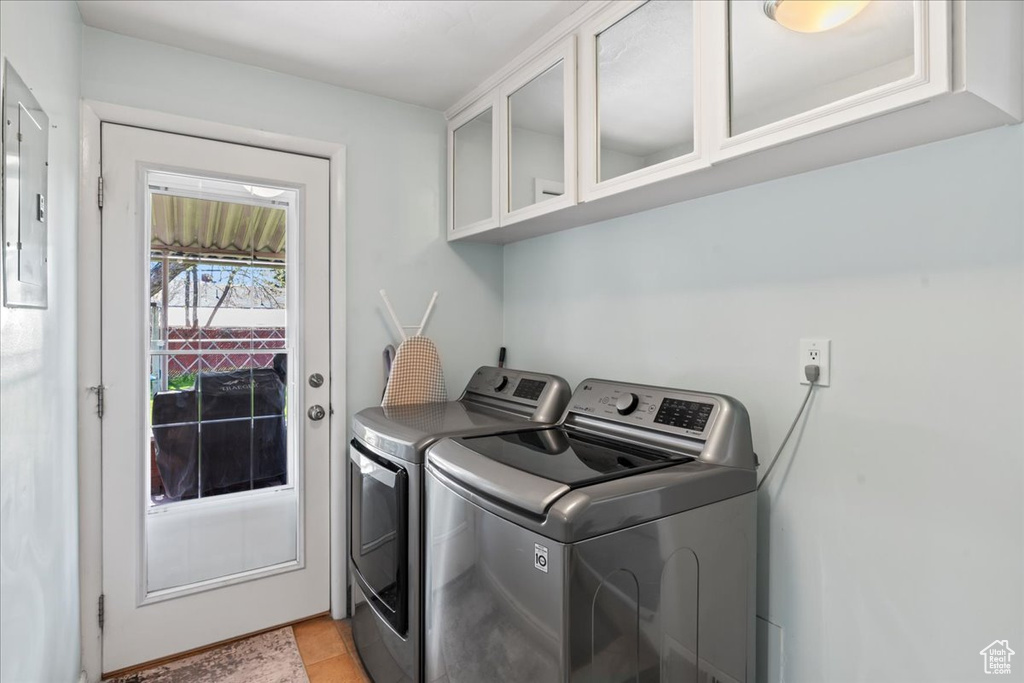 Clothes washing area with light tile flooring, cabinets, and separate washer and dryer