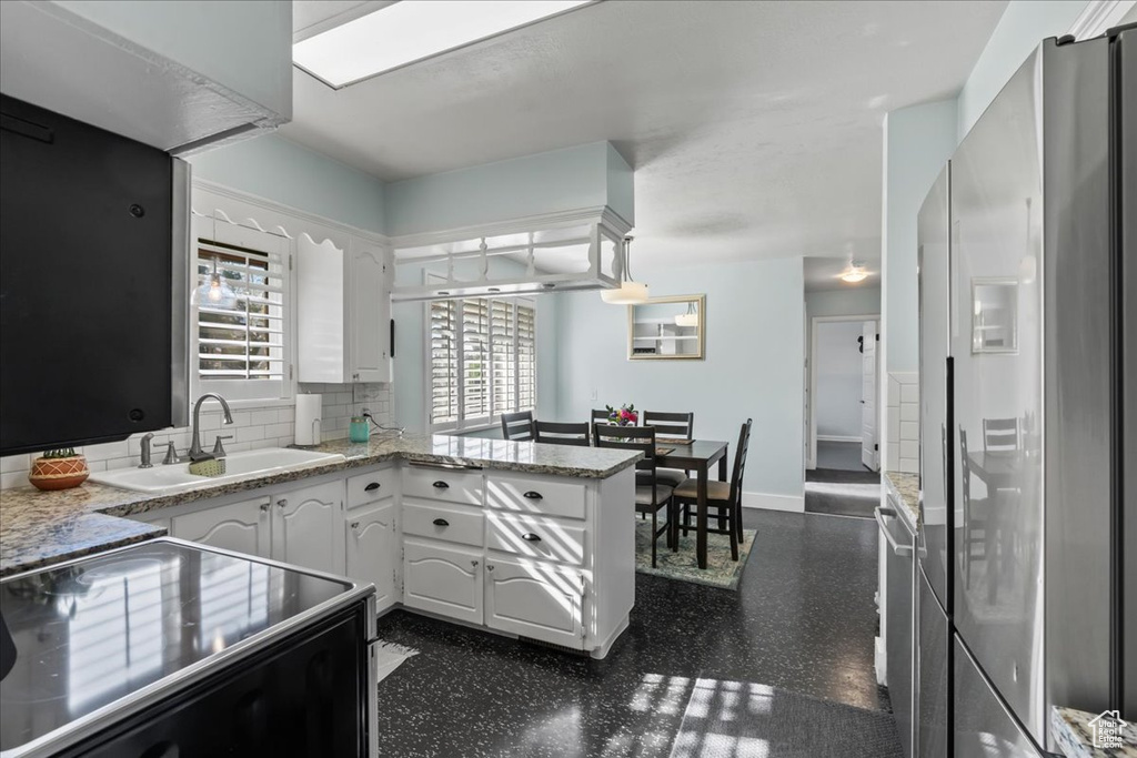 Kitchen featuring white cabinets, sink, tasteful backsplash, stainless steel fridge with ice dispenser, and kitchen peninsula