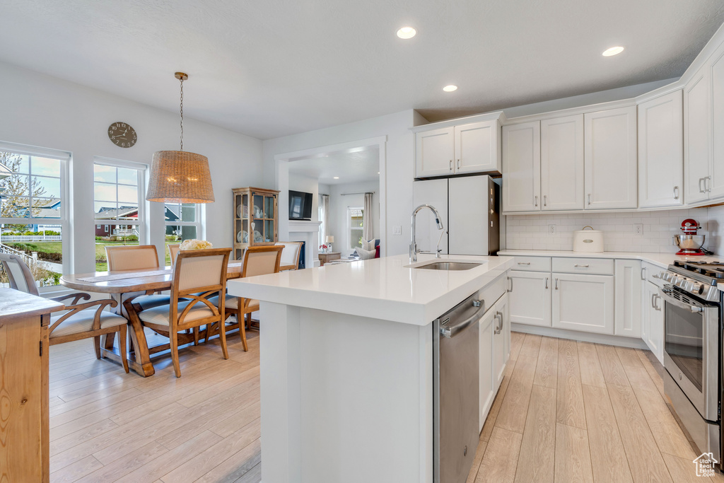 Kitchen featuring hanging light fixtures, white cabinets, stainless steel appliances, tasteful backsplash, and light hardwood / wood-style floors