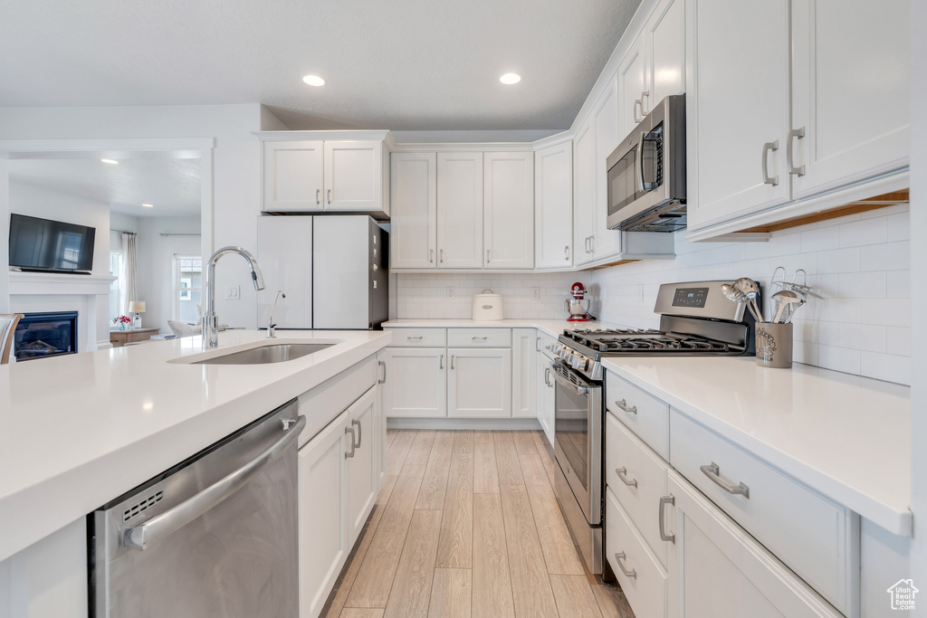 Kitchen featuring white cabinets, sink, backsplash, stainless steel appliances, and light hardwood / wood-style flooring