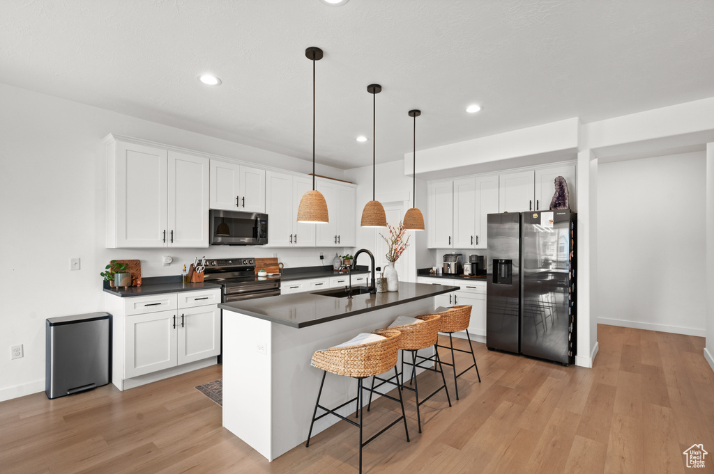 Kitchen featuring light hardwood / wood-style flooring, white cabinetry, black refrigerator with ice dispenser, a center island with sink, and range with electric stovetop