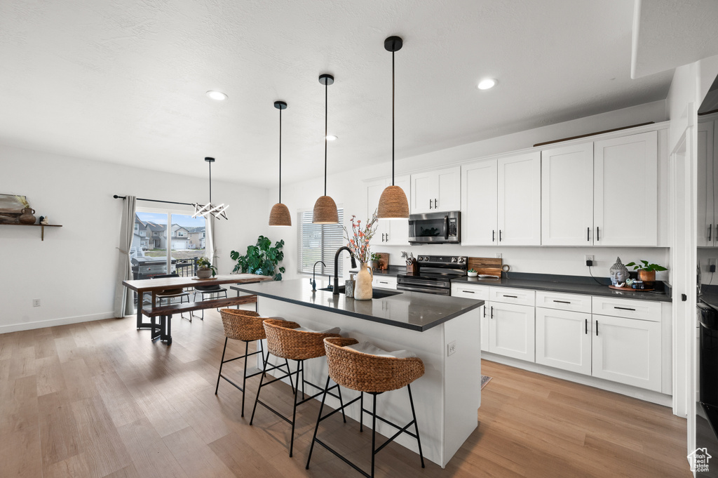 Kitchen with hanging light fixtures, light hardwood / wood-style floors, a kitchen island with sink, sink, and range with electric cooktop