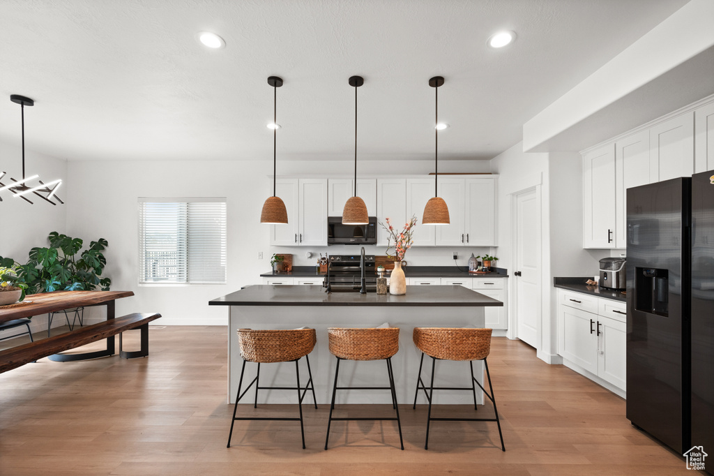 Kitchen featuring hardwood / wood-style flooring, white cabinetry, decorative light fixtures, and black appliances