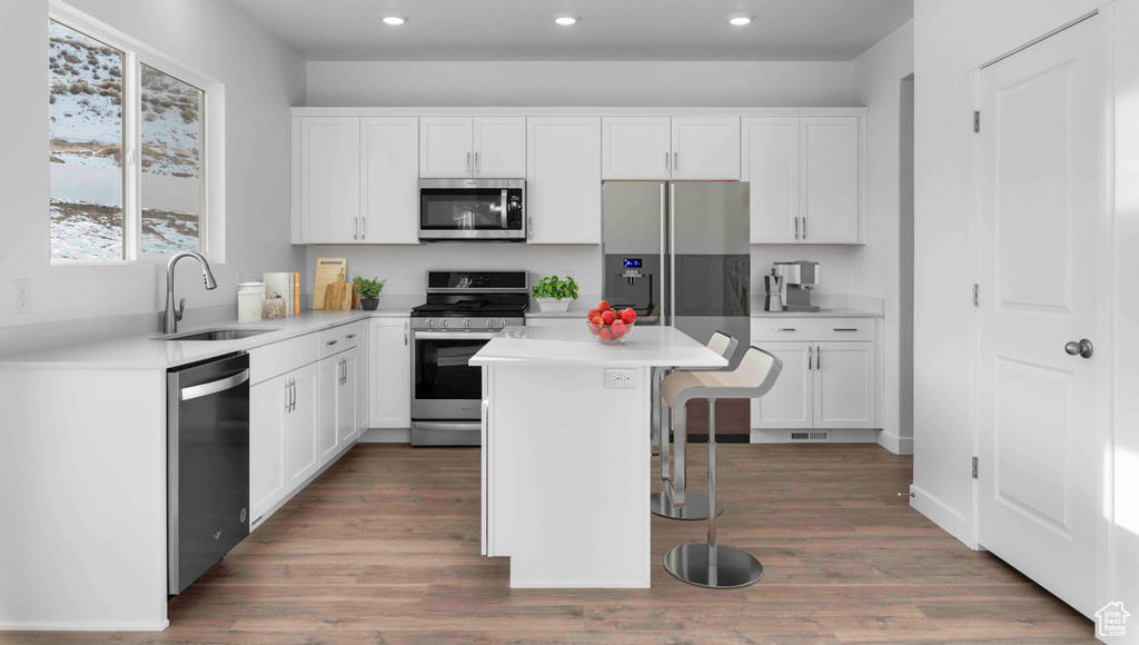 Kitchen with a kitchen bar, appliances with stainless steel finishes, a kitchen island, light hardwood / wood-style floors, and sink