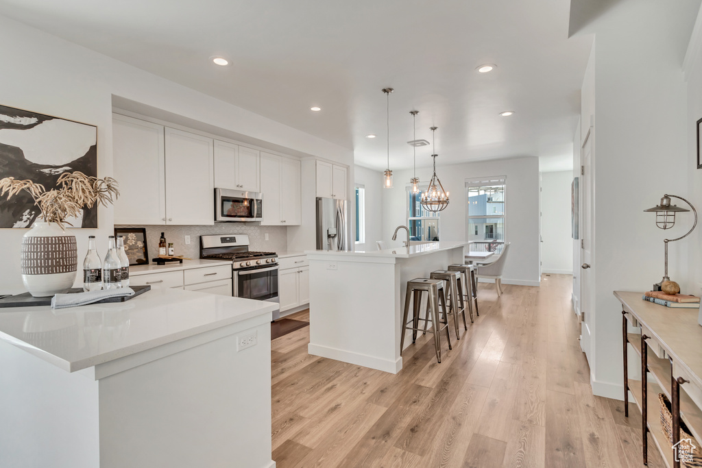 Kitchen featuring light hardwood / wood-style floors, white cabinetry, a spacious island, decorative light fixtures, and stainless steel appliances
