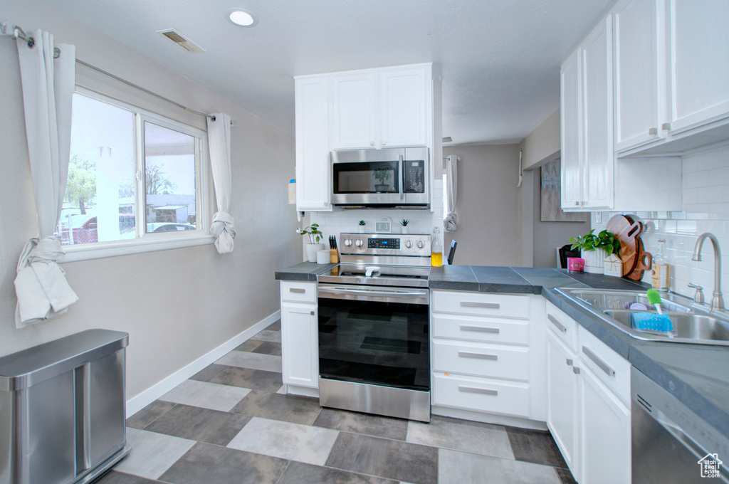 Kitchen featuring white cabinets, backsplash, appliances with stainless steel finishes, light tile floors, and sink