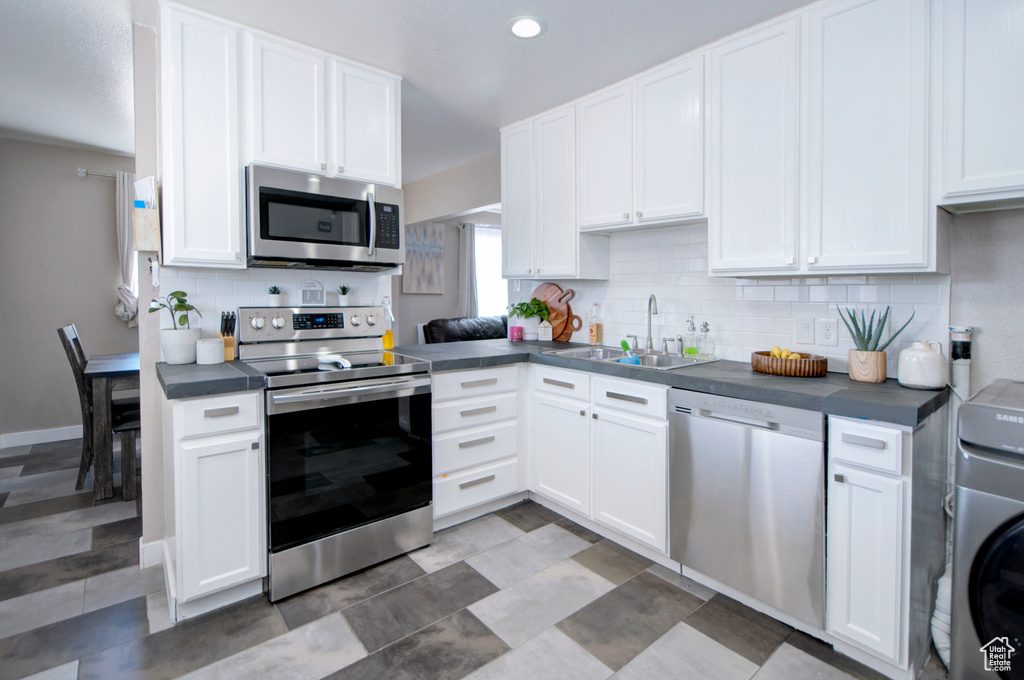 Kitchen with tasteful backsplash, stainless steel appliances, white cabinets, and sink