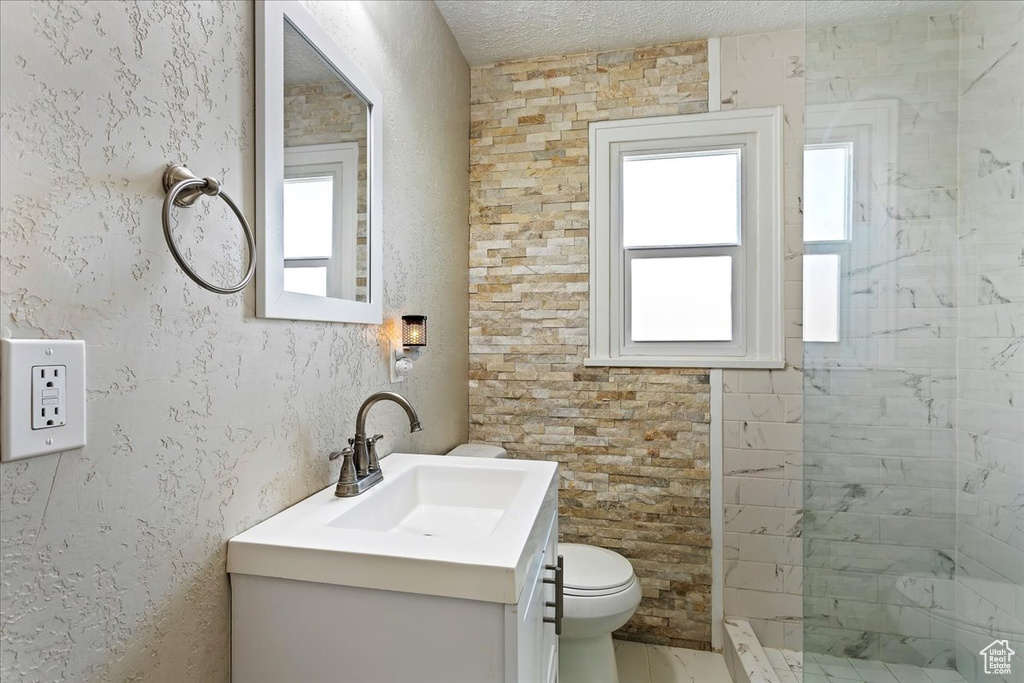 Bathroom featuring a healthy amount of sunlight, toilet, vanity with extensive cabinet space, and a tile shower