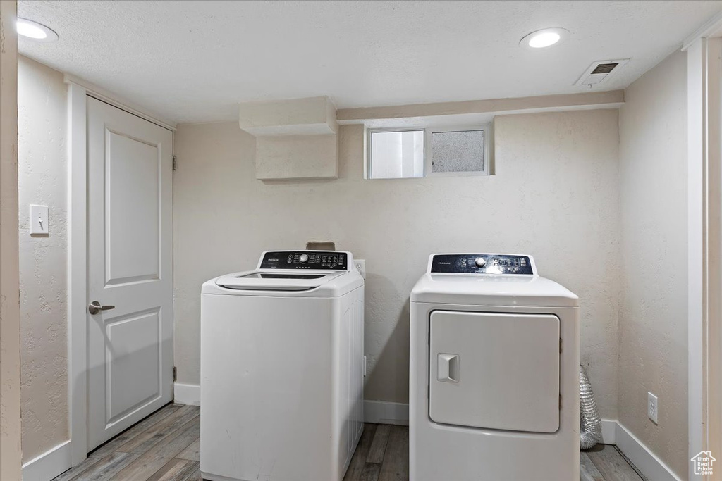 Washroom featuring light hardwood / wood-style floors, washing machine and dryer, and a textured ceiling