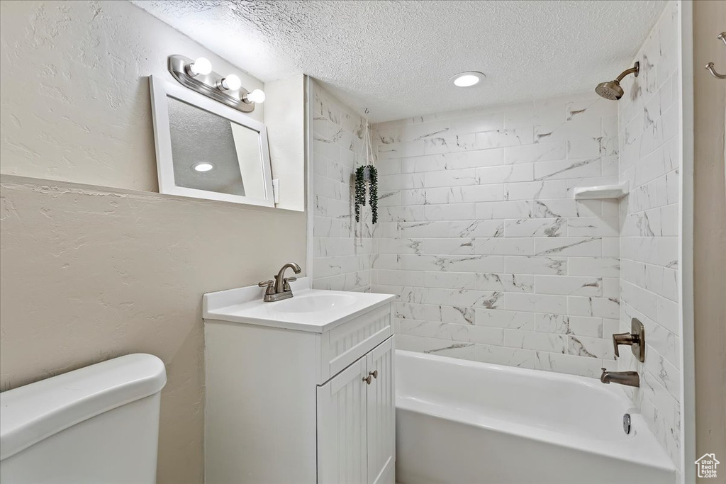 Full bathroom featuring a textured ceiling, vanity, toilet, and tiled shower / bath