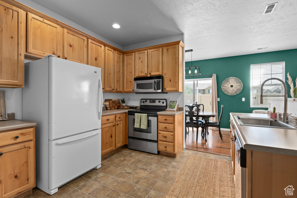 Kitchen featuring decorative light fixtures, sink, appliances with stainless steel finishes, and light tile floors