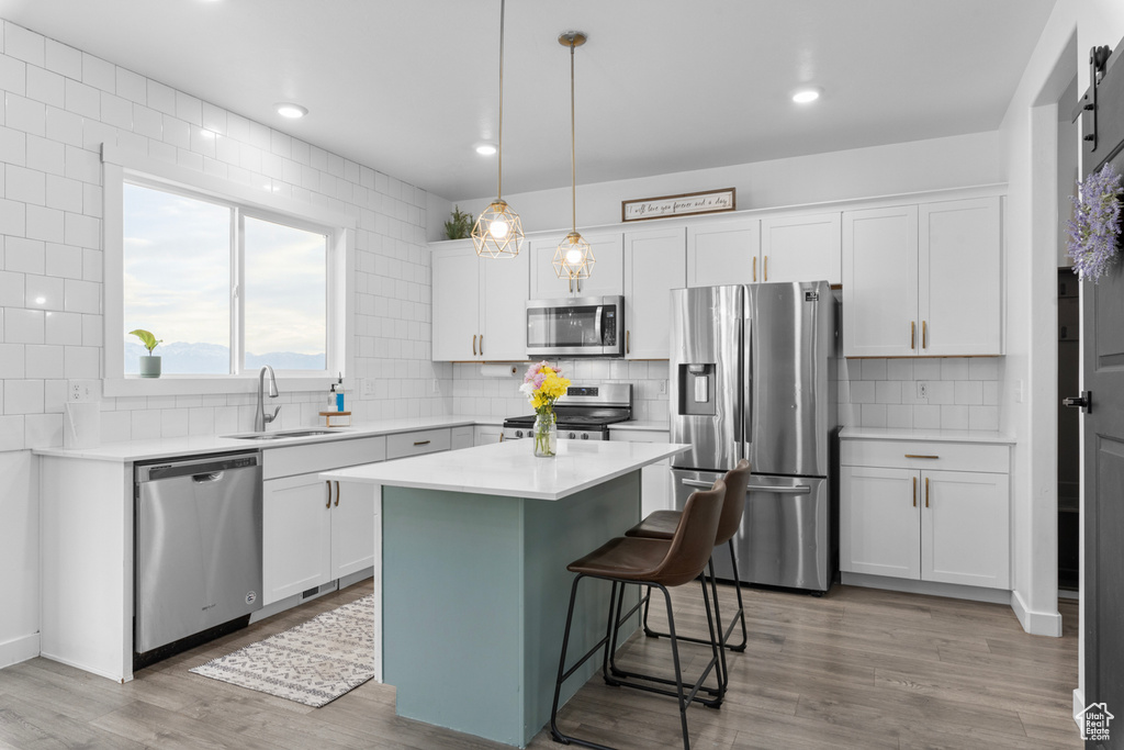 Kitchen featuring a kitchen island, sink, tasteful backsplash, stainless steel appliances, and light hardwood / wood-style flooring