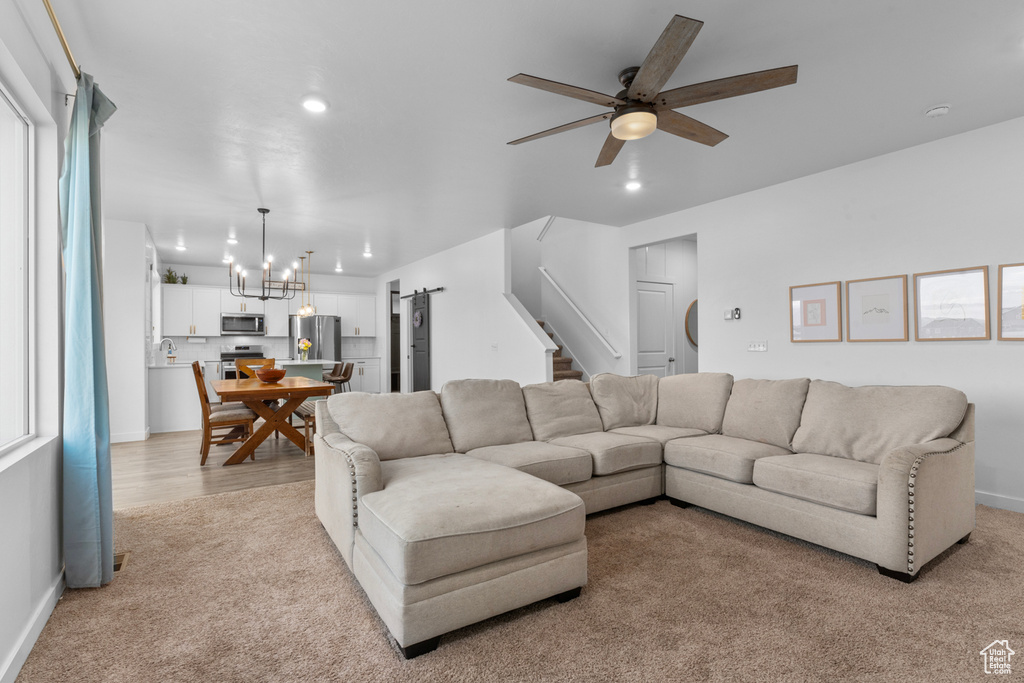 Carpeted living room with ceiling fan with notable chandelier, plenty of natural light, and sink