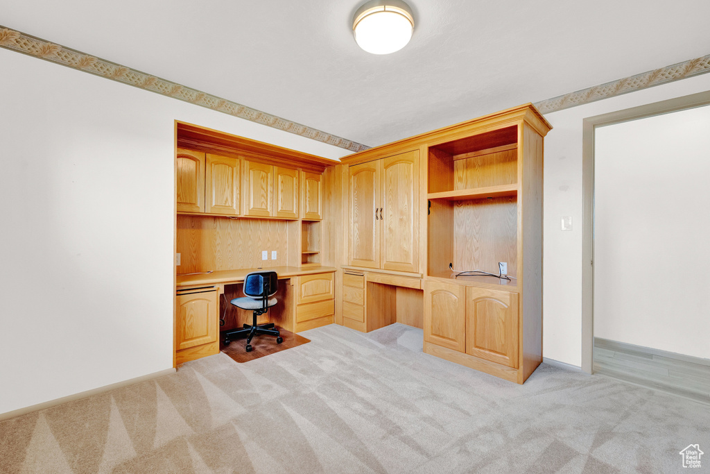 Unfurnished office featuring built in desk and light carpet