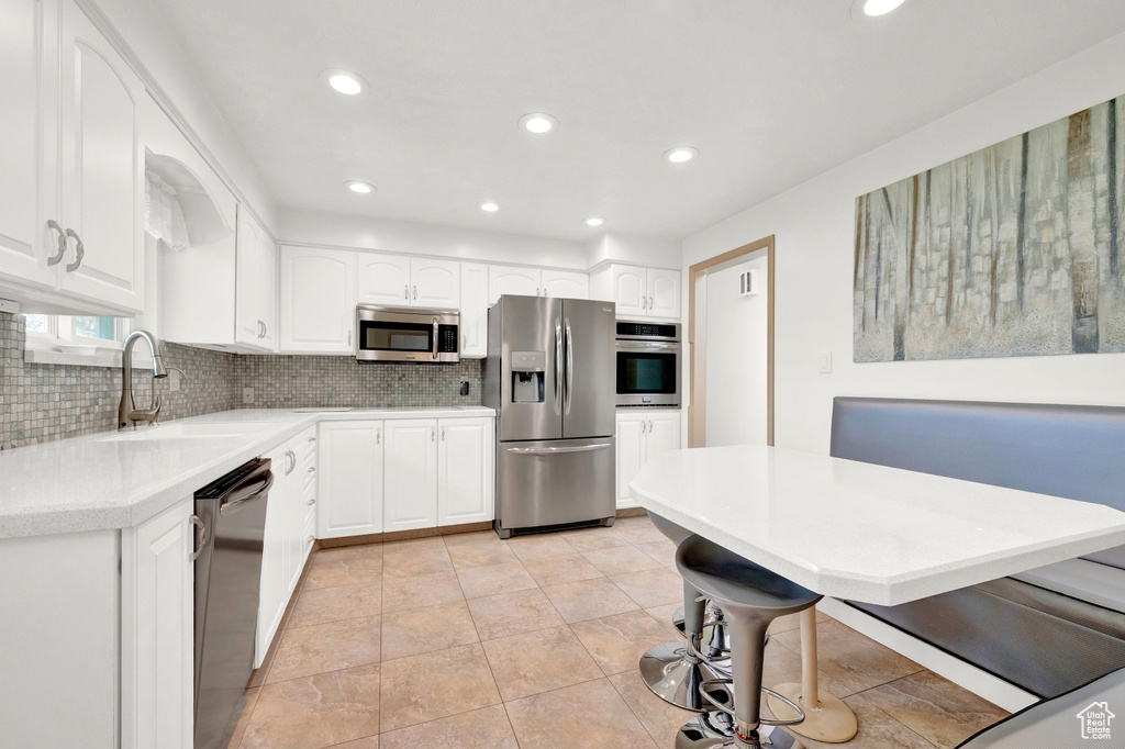 Kitchen with appliances with stainless steel finishes, light tile flooring, backsplash, and white cabinetry