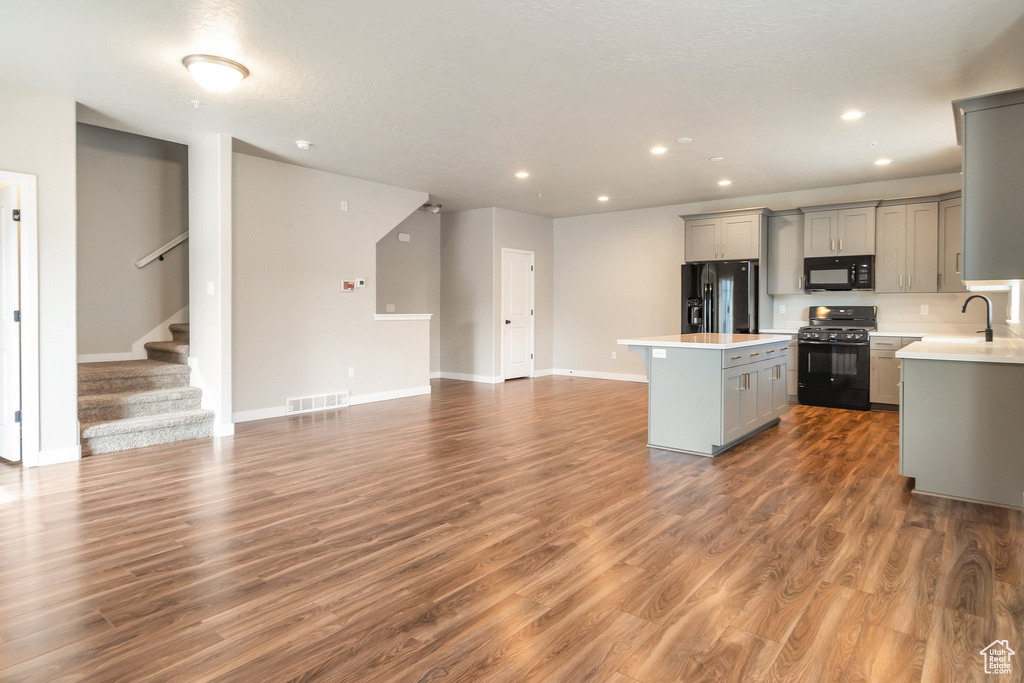 Kitchen with wood-type flooring, gray cabinetry, a center island, and black appliances