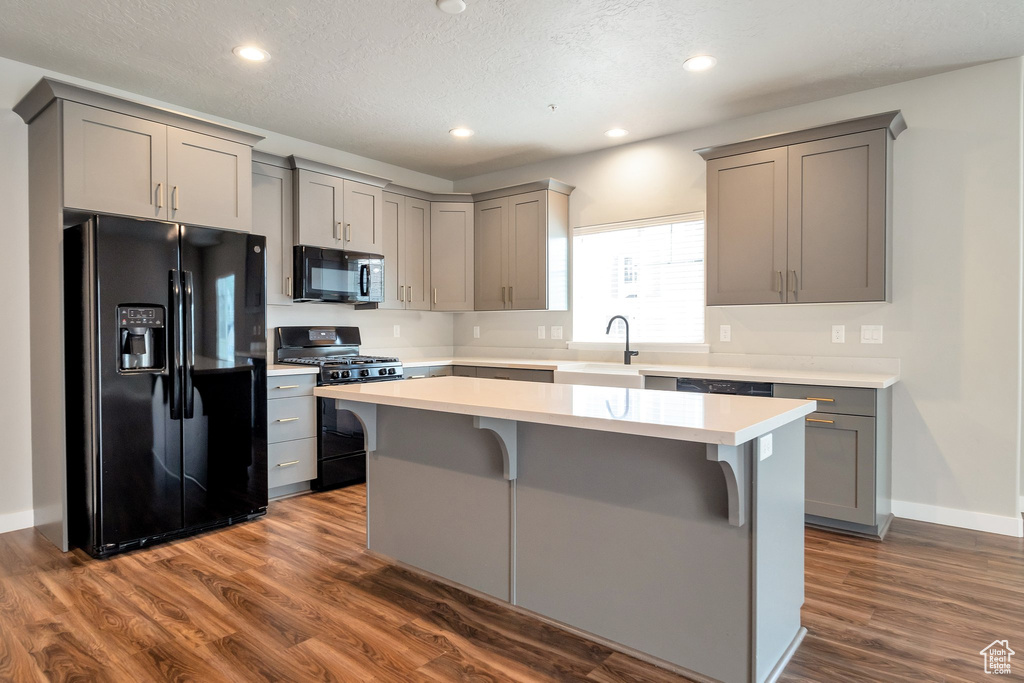 Kitchen with gray cabinetry, a kitchen island, black appliances, and dark wood-type flooring