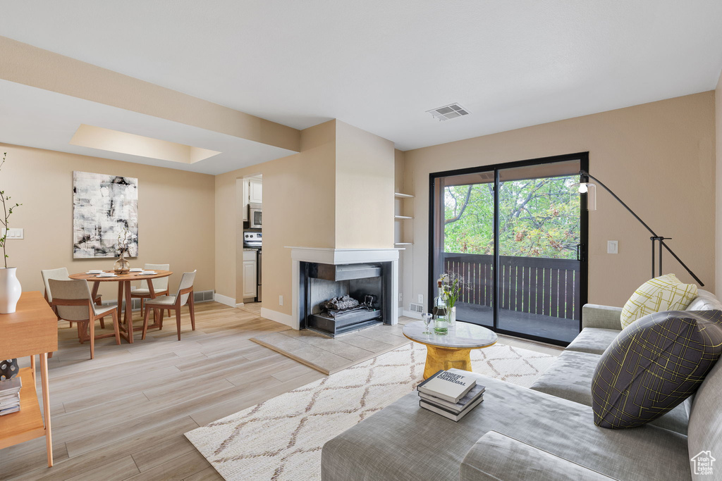 Living room featuring light hardwood / wood-style flooring, a multi sided fireplace, and a tray ceiling