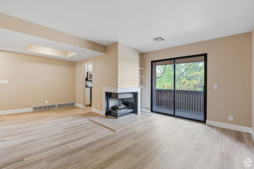 Unfurnished living room featuring light wood-type flooring and a multi sided fireplace
