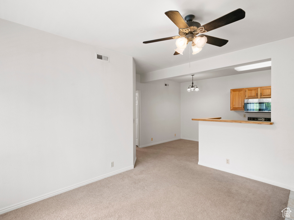 Empty room with ceiling fan with notable chandelier and light colored carpet