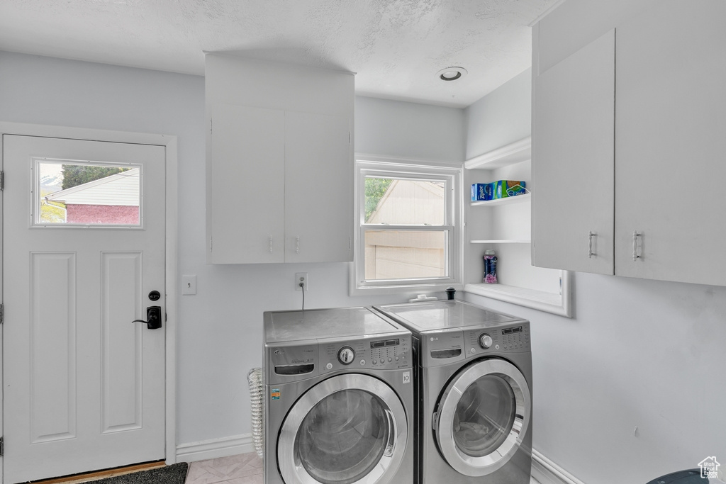 Laundry room with cabinets, washing machine and dryer, and light tile floors