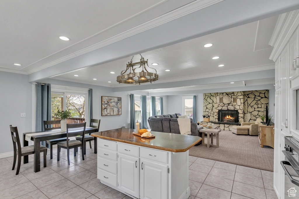 Kitchen featuring a center island, a stone fireplace, white cabinets, oven, and crown molding