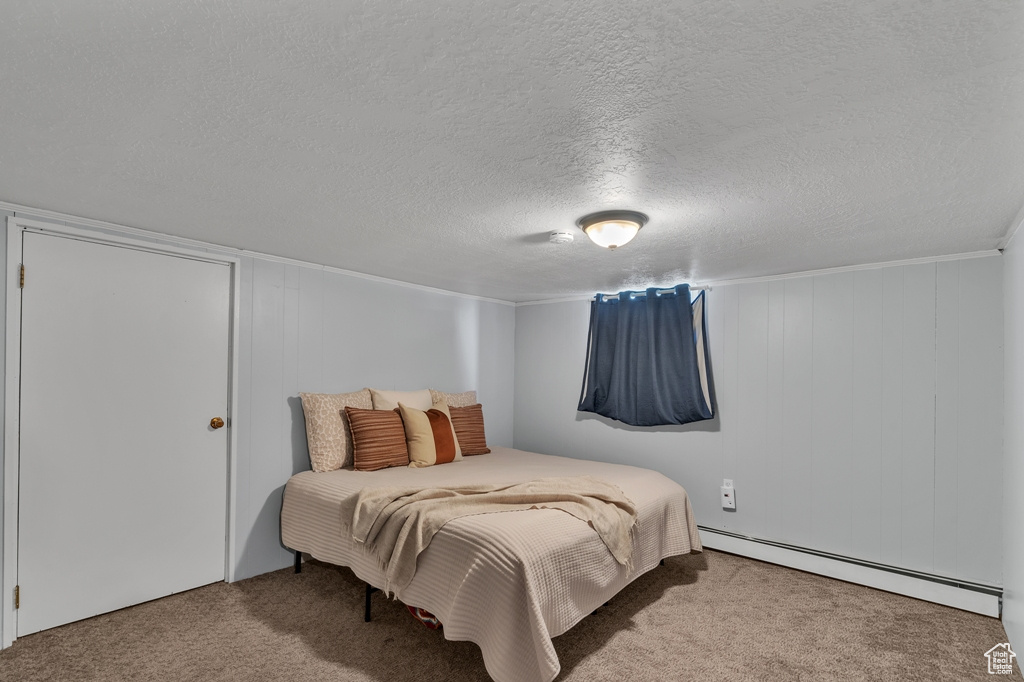 Bedroom with carpet flooring, a baseboard heating unit, and a textured ceiling