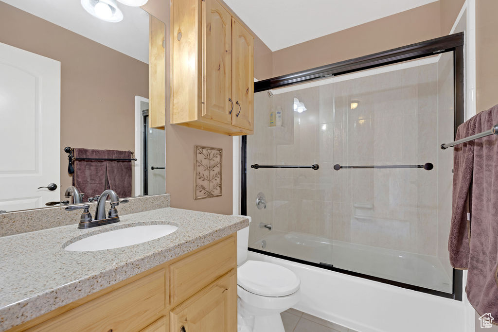 Full bathroom with tile flooring, toilet, combined bath / shower with glass door, and large vanity