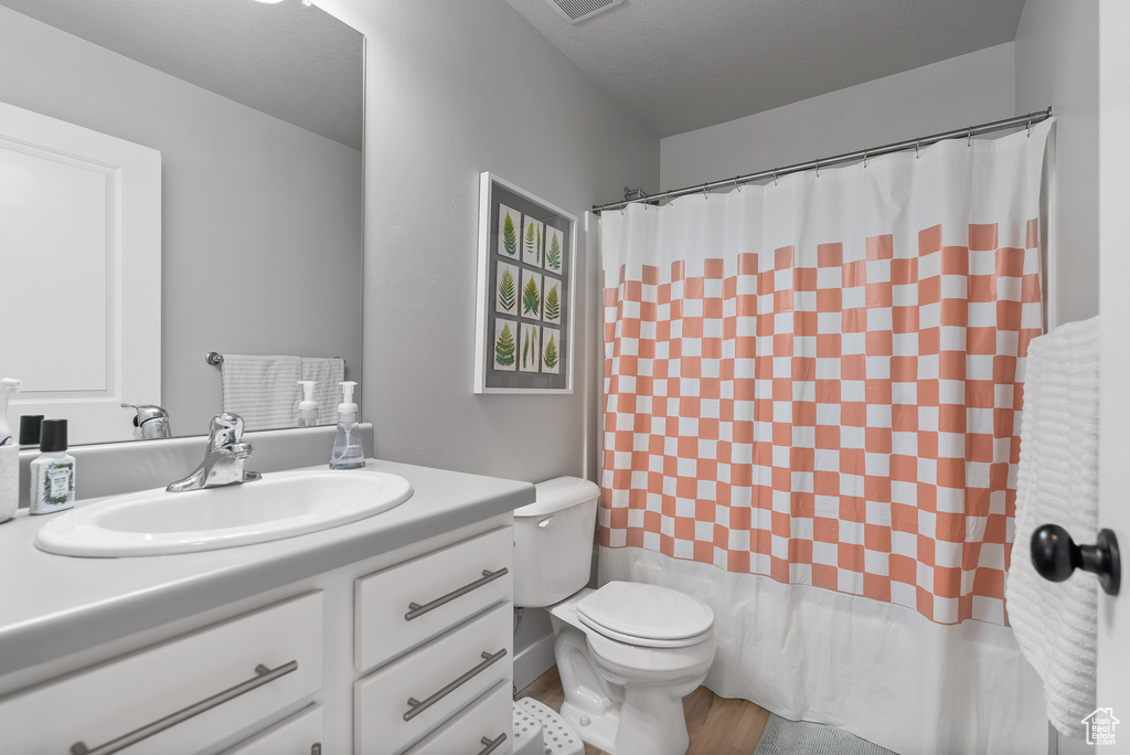 Full bathroom with wood-type flooring, large vanity, shower / bathtub combination with curtain, and toilet